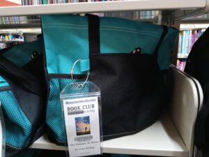 Photograph of a Turquoise and Black Bag with a Book Club in a Bag tag on it.